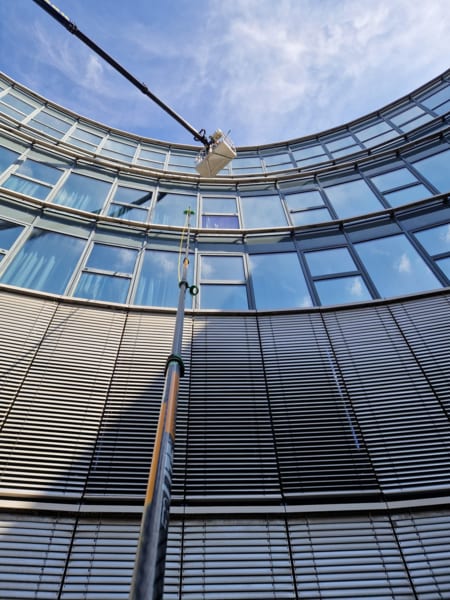 Glasfassade eines Rundbaus wird vom Arbeitskorb aus gereinigt, blauer Himmel