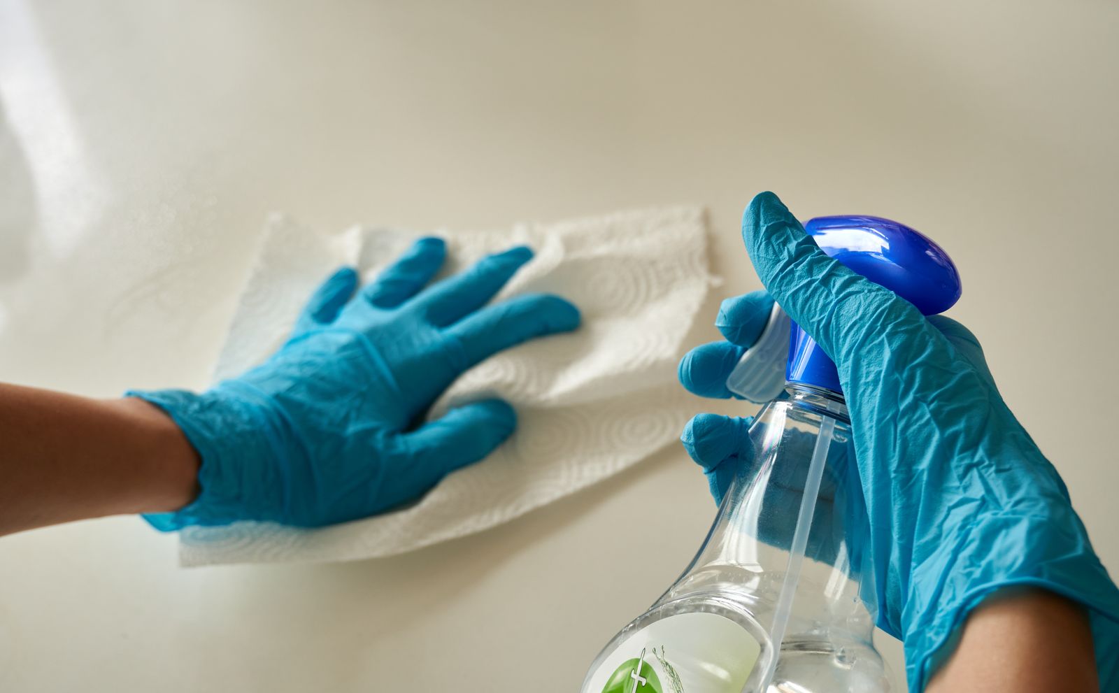 Behandschuhte Hände desinfizieren eine Arbeitsfläche